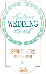 Ein Abzeichen mit einem Lorbeerkranz und der Aufschrift: "Österreichischer Hochzeitspreis. Bronze 2022 Unterhaltung. DJ". Das Design ist in den Farben Türkis und Bronze gehalten, mit einer stilisierten Blume am unteren Rand.